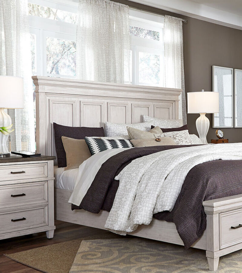 a bedroom with a nightstand next to a wooden, white bed with purple and grey bedding